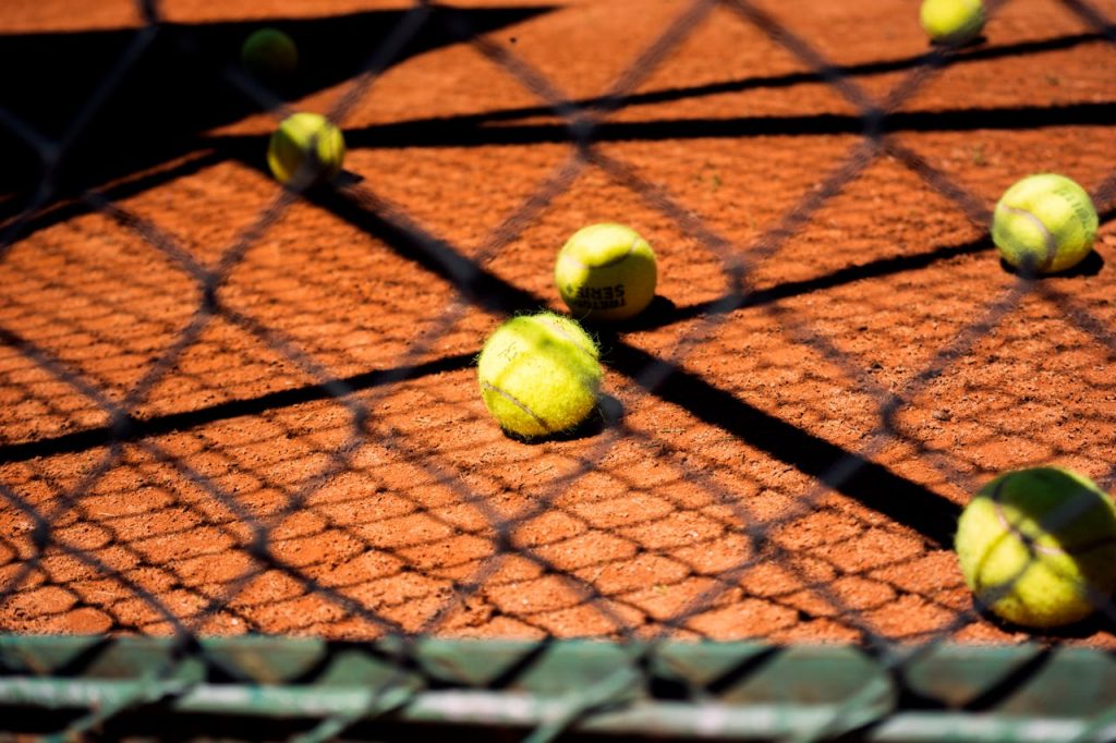 Close-up view of tennis balls scattered on a clay court, captured through a chain-link fence.