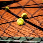 Close-up view of tennis balls scattered on a clay court, captured through a chain-link fence.